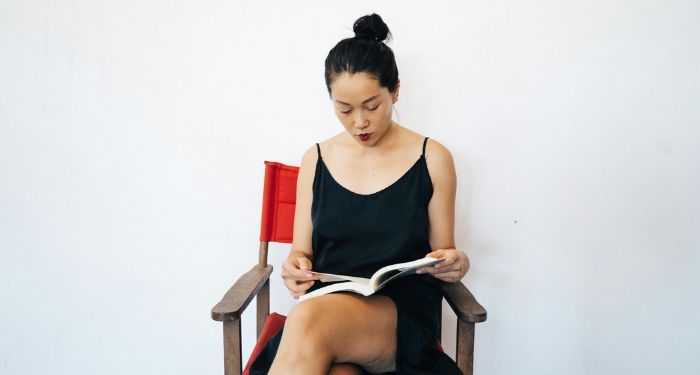 a light tan skinned Asian woman reading a book in a chair.jpg.optimal