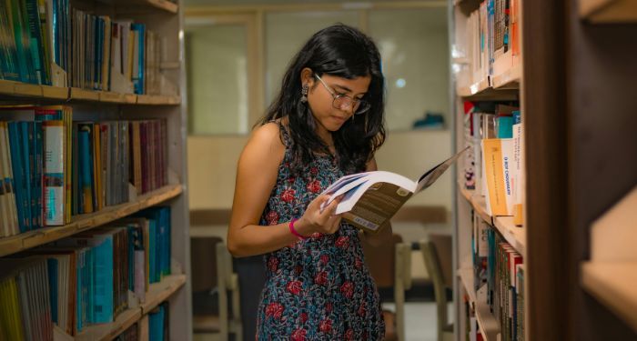 a tanned skin woman of color reading a book in a library.jpg.optimal