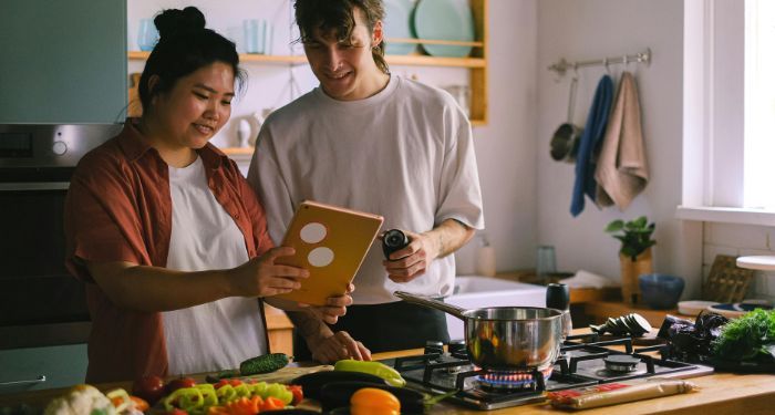 an Asian woman and white man looking at a tablet and cooking in a kitchen.jpg.optimal