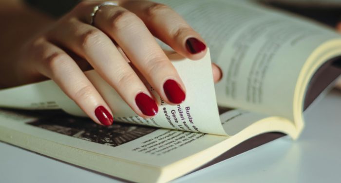 fair skinned hand with red nail polish turns a page in a book.jpg.optimal