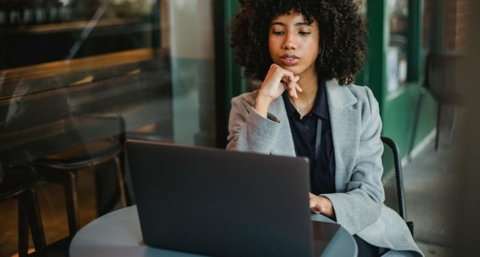 light skinned Black woman with big curly hair on a laptop at a coffee shop.jpg.optimal