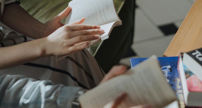 hands of two people reading books with more books on table.jpg.optimal